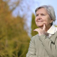 Senior woman looking and smiling in garden on blue sky.