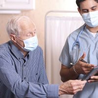 masked senior man talking with healthcare professional