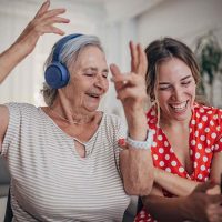 A woman uses headphones to enjoy music with an older woman, one of many creative dementia care tips you can try.