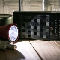 Emergency supplies including a flashlight, batteries, and radio sit at the ready on a table for someone who is prepared for a power outage.