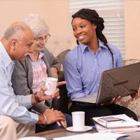 A woman creating a care plan for seniors shows an older couple something on her computer.
