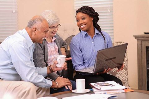 A woman creating a care plan for seniors shows an older couple something on her computer.