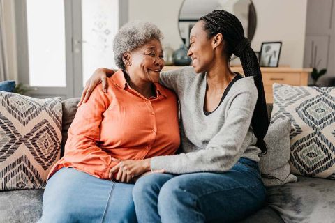 A woman who knows how important it is to support senior independence hugs her mom as they sit on the sofa together.