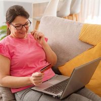 A woman holds a credit card and laptop as she prepares to purchase innovative caregiving solutions.