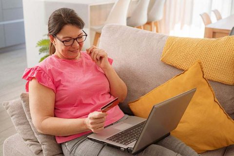 A woman holds a credit card and laptop as she prepares to purchase innovative caregiving solutions.