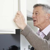 An older man experiencing issues with dementia-related hiding peers into a cabinet.