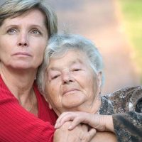 A woman whose mom has dementia gives her a hug while staring thoughtfully into the distance.