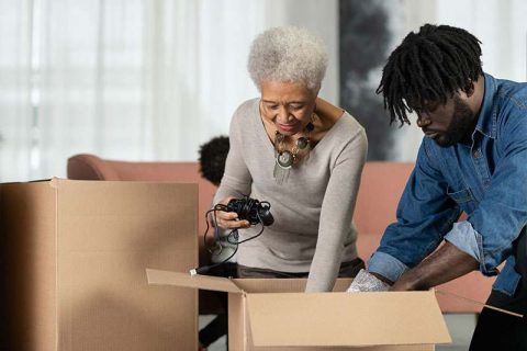 A man knows how important it is to declutter your parents’ home with their help, so he works with his aging mom to pack items into boxes.