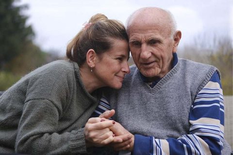 A caregiver holds the hand of an older man who is struggling with Parkinson’s hidden symptoms.