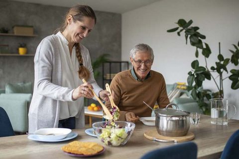 A caregiver helps prevent senior malnutrition for an older man by preparing a healthy meal for him.