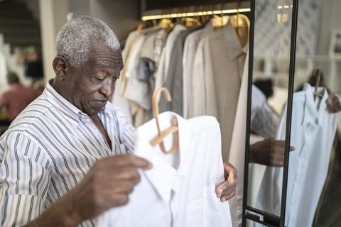 An older man overcomes dementia dressing challenges as he selects a shirt from his closet.