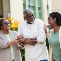 A woman meeting the care needs of both parents joins them for a walk.