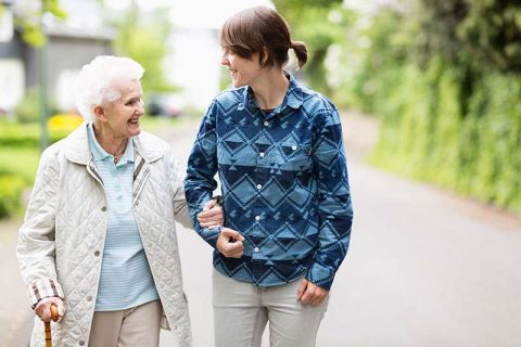 A caregiver committed to reducing fall risks for older adults steadies an older woman as they go for a walk.