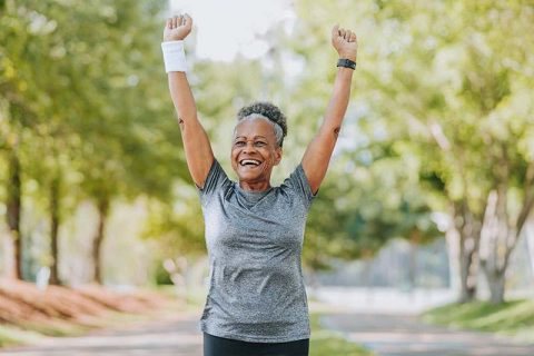 An older woman raises her hands triumphantly after reaching a goal, understanding the importance of goal setting for older adults.