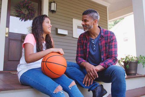 A man who knows what to say when kids have questions about dementia listens attentively to his daughter as they sit together on the front porch.