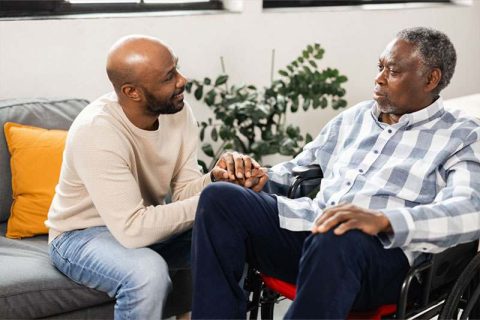A man holds his father’s hand as he considers ways to address environmental triggers for dementia.