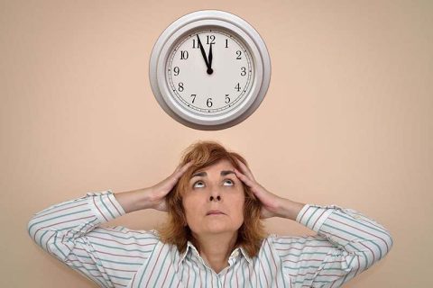An overwhelmed woman glances at the clock overhead as she prepares to implement the 5-minute rule for caregivers.