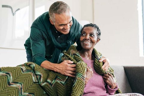 A man utilizing effective Alzheimer’s care tips smiles as he wraps a blanket around his wife’s shoulders.