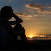 The silhouette of a person watching the sunset represents feelings of caregiver guilt after loss.