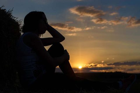 The silhouette of a person watching the sunset represents feelings of caregiver guilt after loss.