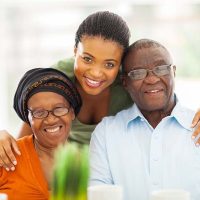 A woman caring for aging parents with different needs smiles as she places an arm around her parents’ shoulders.