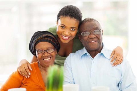 A woman caring for aging parents with different needs smiles as she places an arm around her parents’ shoulders.