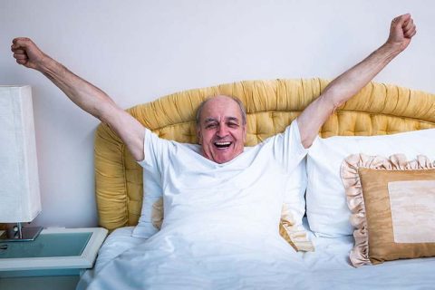 A man who tried tips for better sleep for seniors stretches and smiles as he wakes up refreshed.