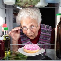 A woman stares at a donut in her fridge, experiencing the addictive link between older adults and processed foods.