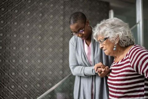 A woman displaying some of the signs of early Alzheimer’s receives a helping hand from her caregiver.