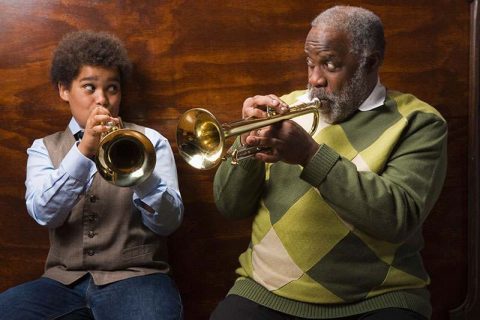 A boy plays a trumpet with his family member, a great way to support your parent’s cognitive health through music.