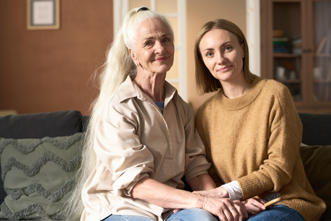 A woman holds the hands of her caregiver as they discuss Alzheimer’s coping strategies.
