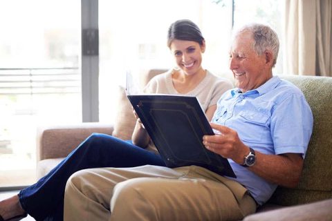 A man enjoys reminiscing with his caregiver as they look through a photo album together.