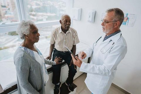 A woman reassures her husband as she looks concerned that the doctor isn’t listening.